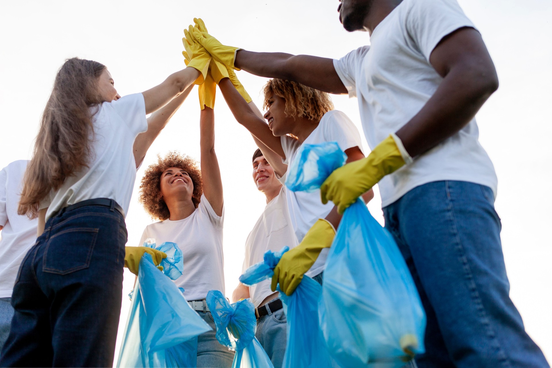 team of volunteers in gloves and with garbage bags rejoice together at success and high five